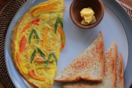 a plate of food with a omelet and a bowl of butter at Nirwa 1 Ubud Guesthouse in Ubud