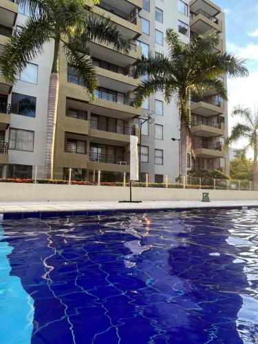 a pool with palm trees in front of a building at Comfortable Apto en Hacienda Peñalisa in Ricaurte
