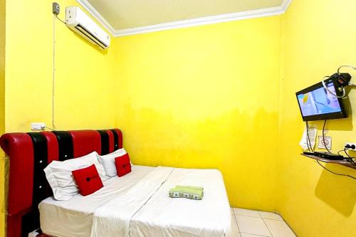 Cette petite chambre jaune comprend un lit et une télévision. dans l'établissement Hotel Alam Lestari RedPartner, à Palembang