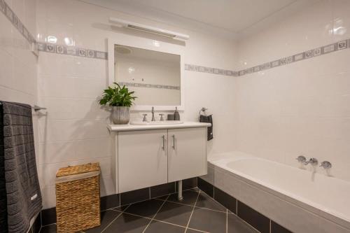 a bathroom with a sink and a tub and a mirror at La Ronde One - Unit 1 - oceanstays in Yamba