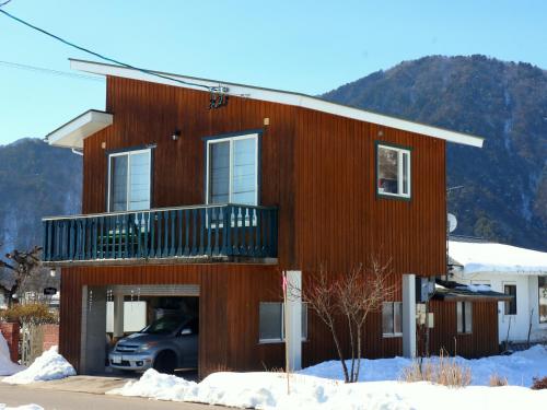 een houten huis met een balkon in de sneeuw bij コテージ野の香 in Omachi