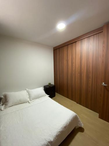 ein Schlafzimmer mit einem weißen Bett und einer Holzwand in der Unterkunft Apartamento en Retiro in El Retiro