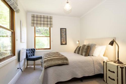 a white bedroom with a bed and a chair at Stags Head Cottage-cosy cottage with hot tub in Arrowtown