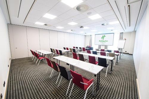 a conference room with tables and chairs and a screen at Holiday Inn Lübeck by IHG in Lübeck