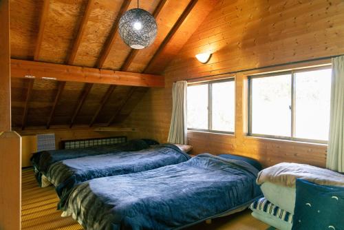 two beds in a room with wooden walls and windows at 千葉の静かな山の中の貸切コテージ 鴨川コテージ in Kamogawa
