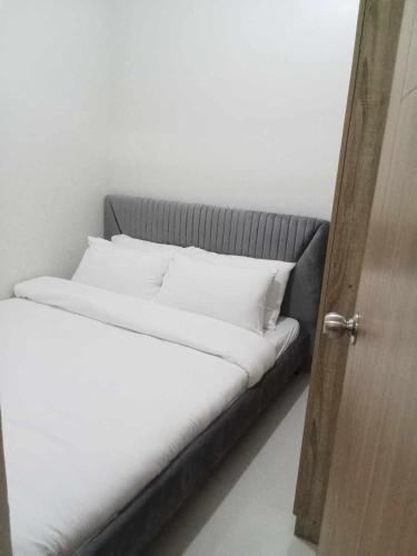 uma cama com lençóis brancos e almofadas ao lado de uma porta em JM Suite at LovetoStay em Manila