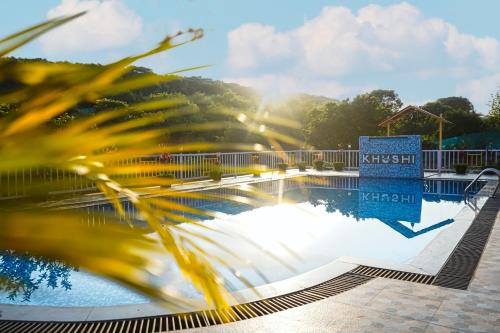 a swimming pool with a palm tree in the foreground at Khushi Riverside Resort & Spa in Mahabaleshwar