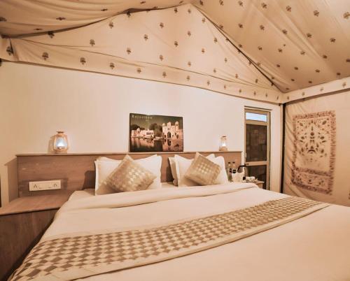 Griat sandy desert camp jaisalmer في جيلسامر: غرفة نوم بسرير كبير عليها شراشف ووسائد بيضاء