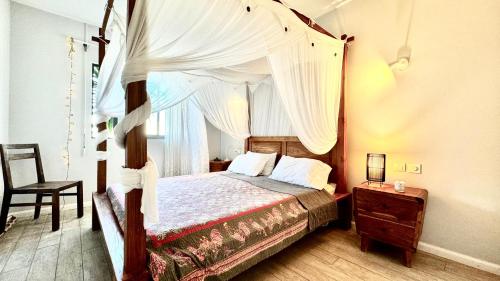 a bedroom with a canopy bed and a chair at Appartement 2 Chambres Grande Piscine et Proche de la Plage in Tamarin