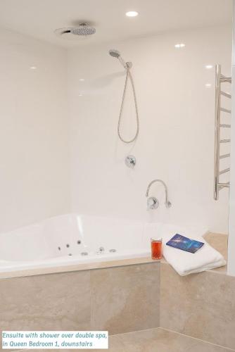a bath tub with a shower and a book on a table at Peaceful Places - Surf Side, Linen, Pets, Wifi in Inverloch
