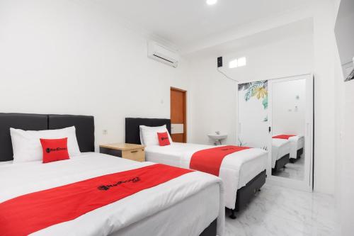 a bedroom with three beds with red and white sheets at RedDoorz Syariah @ Sakura Hotel Jatiwaringin in Bekasi