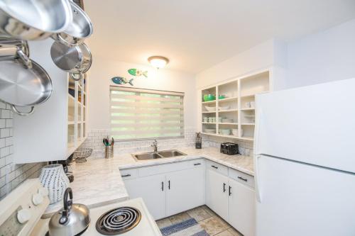 a kitchen with white cabinets and a sink and a refrigerator at Casa Posada - So Close You Can Hear the Waves Historic Beach Cottage w Beach Gear in Anna Maria