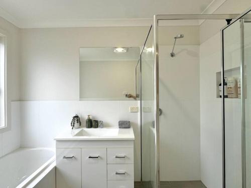 y baño blanco con lavabo y ducha. en Canberra Comfort Family Cottage with 5 Beds& Pet Welcoming, en Hall