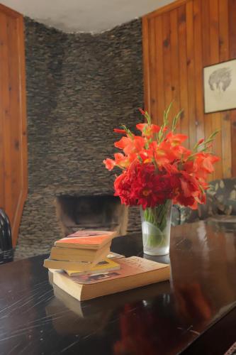 a vase of red flowers sitting on a table with books at Cedar Lodge By Aahma in Rāmgarh