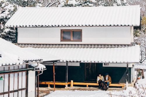 two people sitting on a porch of a house in the snow at サウナ付き一棟貸し宿 大岡辻-tsuji oooka- in Ookanakamaki
