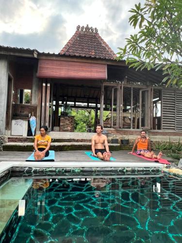three people sitting on mats in front of a swimming pool at PINOKKIO B&B Restaurant in Jimbaran