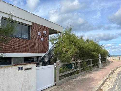 a brick house with a white fence next to the beach at Villa d'architecte - Les Pieds dans l'Eau in Ver-sur-Mer