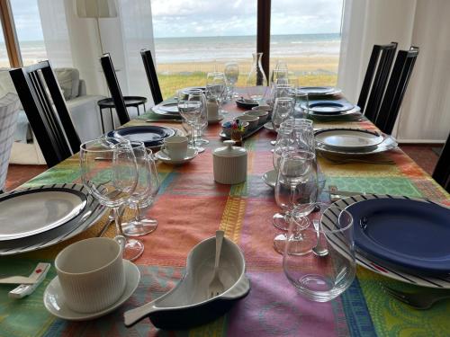 a table with glasses and plates on it with the ocean in the background at Villa d'architecte - Les Pieds dans l'Eau in Ver-sur-Mer