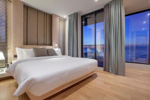a bedroom with a large white bed and large windows at Balcony Seaside Sriracha Hotel & Serviced Apartments in Si Racha
