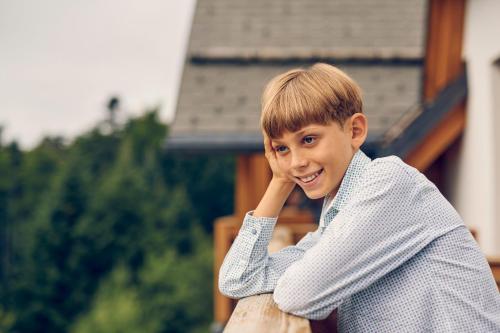 a young boy sitting on a fence with his hand on his face at Pohorje Village Wellbeing Resort - Forest Hotel Videc in Pohorje