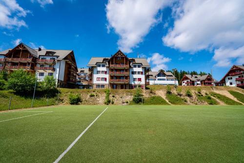 una pista de tenis con casas al fondo en Pohorje Village Wellbeing Resort - Forest Apartments Videc, en Hočko Pohorje