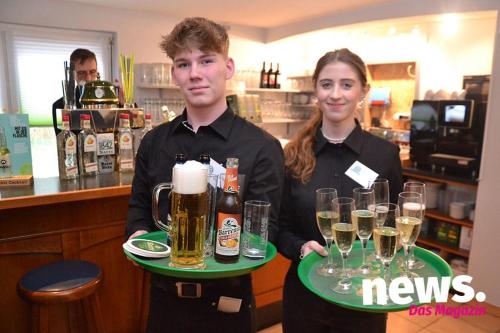 Un uomo e una donna che tengono in mano un vassoio di bicchieri da champagne di Gasthaus und Pension Zur alten Fähre a Porta Westfalica