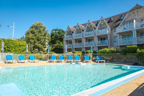 une piscine avec des chaises bleues et un bâtiment dans l'établissement Les Glénans - Duplex vue mer proche plage, à Bénodet