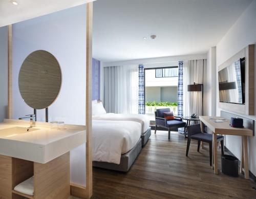 a hotel room with a bed and a sink and a mirror at Novotel Chiangmai Nimman Journeyhub in Chiang Mai