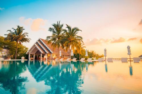 a resort swimming pool with a house and palm trees at LUX* South Ari Atoll Resort & Villas in Maamigili