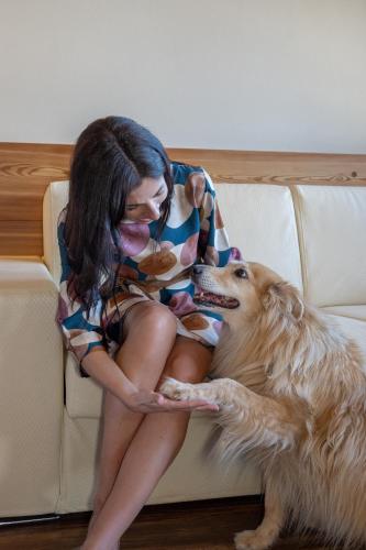 a woman sitting on a couch with a dog at Belvedere Dolomites Flower Hotel in Moena