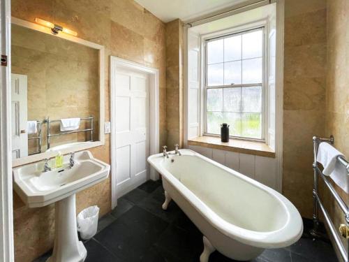 a bathroom with a tub and a sink and a window at Colzium Farmhouse in Blitterlees