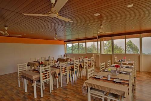 uma sala de jantar com mesas, cadeiras e janelas em Hill View Resort Munnar em Anachal