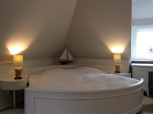 a bedroom with a white bed with two lights on it at Teewelkenhüs Schwalbennest in Archsum