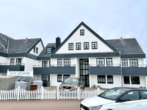 uma casa branca com carros estacionados em frente em Atlantik 23 -Standnahe Ferienwohnung em Wenningstedt