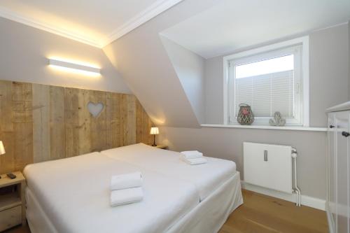 ein weißes Schlafzimmer mit einem Bett und einem Fenster in der Unterkunft Kiebitz-Nordseebrise - Wenningstedt in Wenningstedt-Braderup