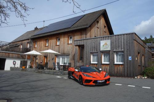 pomarańczowy samochód zaparkowany przed drewnianym budynkiem w obiekcie Speedys Gästehaus w mieście Baar