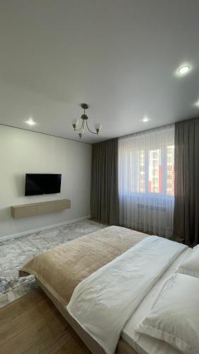 a white bedroom with a large bed and a television at Bekzat Apartment in Atyrau