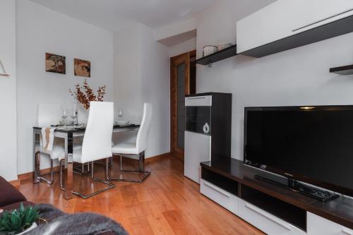 sala de estar con TV y mesa con sillas blancas en tuGuest Dílar Apartment, en Granada