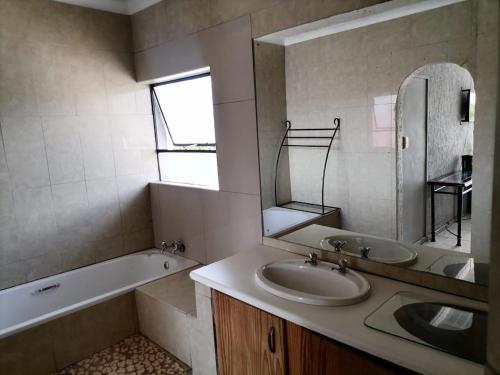 a bathroom with a sink and a tub and a mirror at Eeufees Guesthouse in Bloemfontein