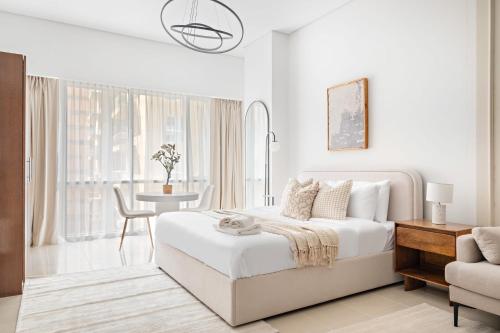 een witte slaapkamer met een bed, een tafel en een stoel bij Silkhaus Modern Studio Near Silicon Central Mall in Dubai