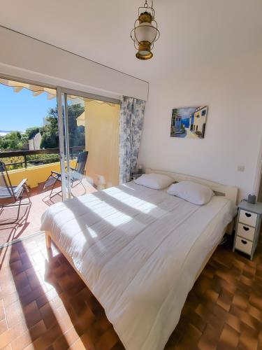 une chambre avec un grand lit blanc et un balcon dans l'établissement Les Marguerites - T2 avec clim et parking à la Fossette, au Lavandou
