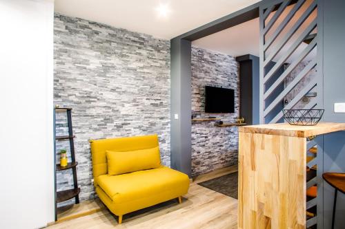 a yellow chair in a room with a brick wall at Homey Cute - Parking inclus - Proche Geneve in Annemasse