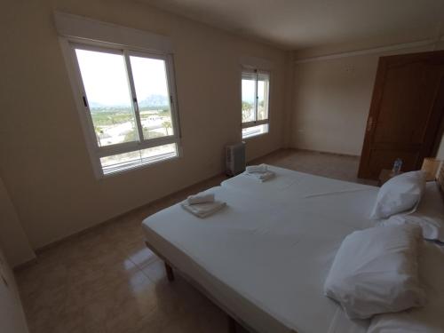 a bedroom with a large white bed with two windows at Hotel Algorfa in Castillo de Montemar