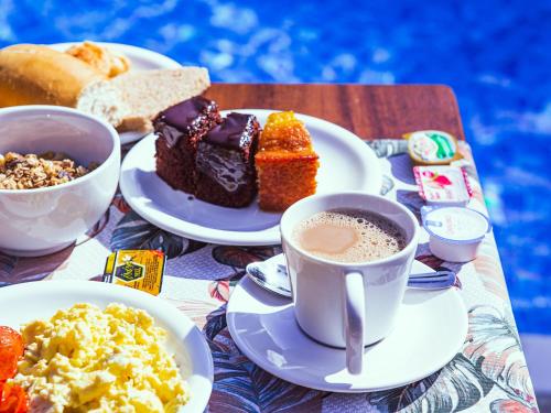 einen Tisch mit Teller mit Speisen und Tassen Kaffee in der Unterkunft VELINN Pousada Canoa Ilhabela in Ilhabela