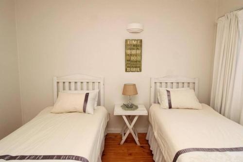 two beds in a room with a table with a lamp at Lazy Days in Natureʼs Valley