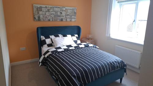 a bedroom with a bed with a blue headboard and a window at Tropical Sun Homes - Beautiful spacious 3 bed home in a serene environment with free parking for 2 cars in Manchester