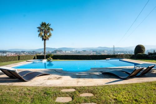 una piscina con 2 tumbonas y una palmera en Casa Tranquilidade - Casa moderna com piscina en Guimarães