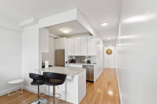 a white kitchen with a counter and two black chairs at Flat In The Bush in Brooklyn