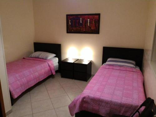 two beds in a room with pink sheets at B&B PIAZZA KOLBE in Acquaviva delle Fonti