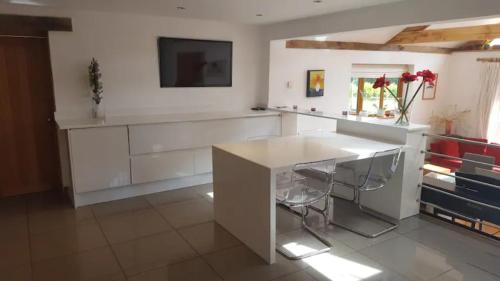 a kitchen with white cabinets and a table with stools at Prestwick Oak - 3 Kingsize Ensuites - Openplan Contemporary Rural Garden in Chiddingfold